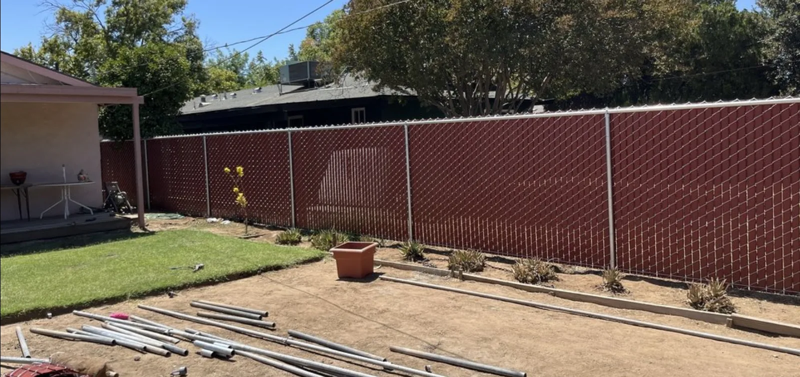 Brown privacy-slat chain-link fence newly installed by AR Fence around a residential backyard, with galvanized posts and spare fence pipe still laid out on the ground
